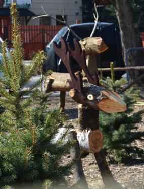 fából faragott kis szarvas a kertvárosi tanyaudvar fenyői között