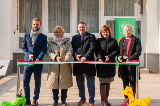 Dénes Hilda intézményvezető, Kovács Péter polgármester, Ács Anikó alpolgármester, Simon Mariann önkormányzati kapcsolattartó és a kivitelező képviselője átvágják a nemzeti színű szalagot a Gyerekkuckó Óvoda átadóján.