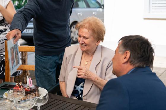 Manyi néni képeket mutat az unokáiról a polgármesternek